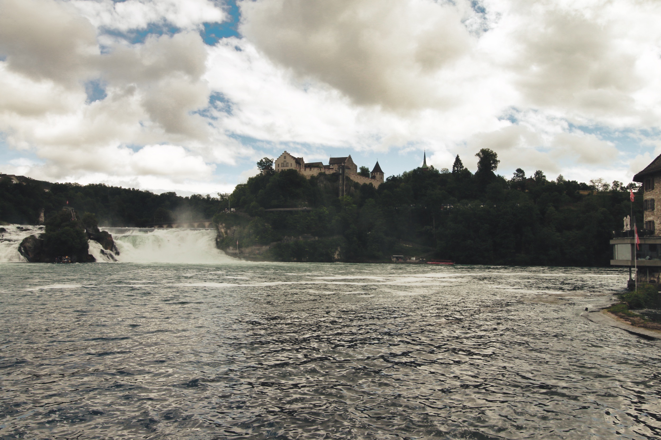 מפלי מים גועשים וטירה על גבעה מיוערת תחת שמיים מעוננים | Rushing Waterfalls and a Castle on a Wooded Hill under Cloudy Skies
